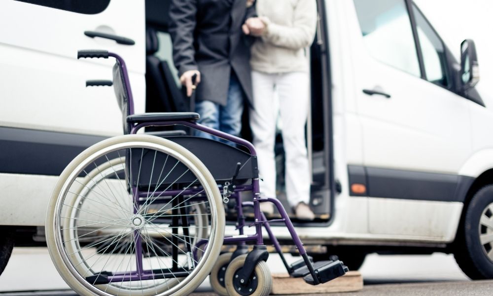 A wheelchair stands beside an accessible van as two passengers step out.