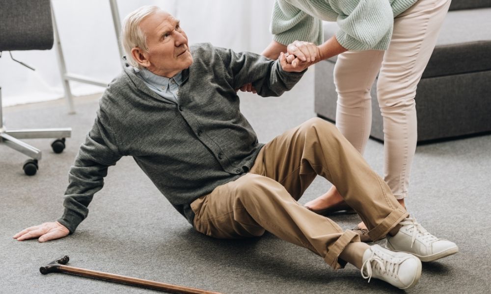 A caregiver helps an older man rise from the floor after a fall.