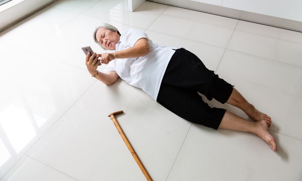 An older woman lies on the floor near her cane after a fall.